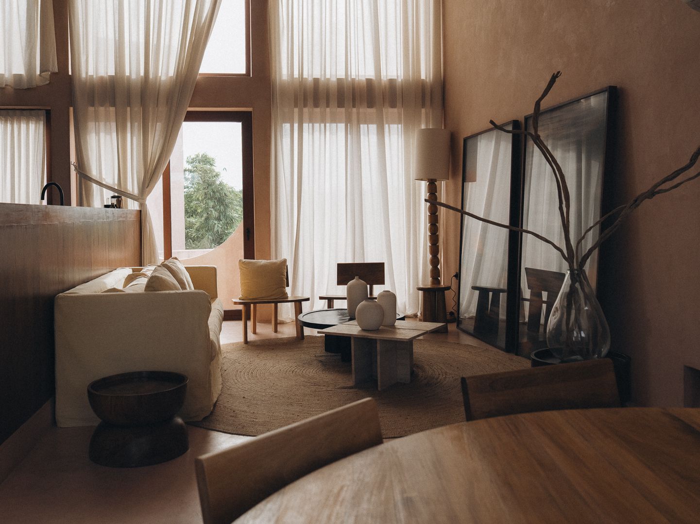 A double-height living room with sheer floor-to-ceiling curtains, a linen sofa, and a pair of leaning mirrors